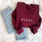 maroon crewneck sweatshirt with embroidered mini dental icons across the chest in white thread styled with blue jeans