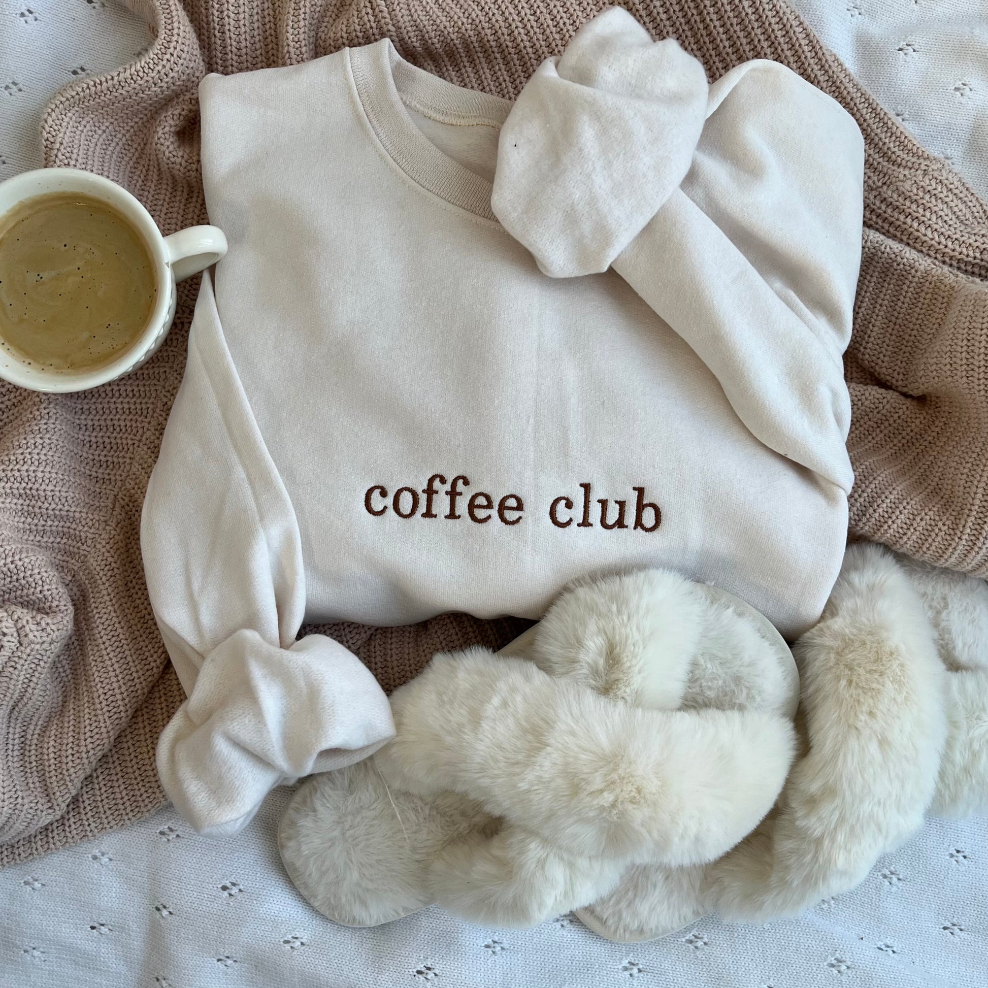 styled flat lay of a sweet cream crewneck sweatshirt with embroidered coffee club across the chest in chestnut  thread