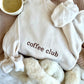 styled flat lay of a sweet cream crewneck sweatshirt with embroidered coffee club across the chest in chestnut  thread