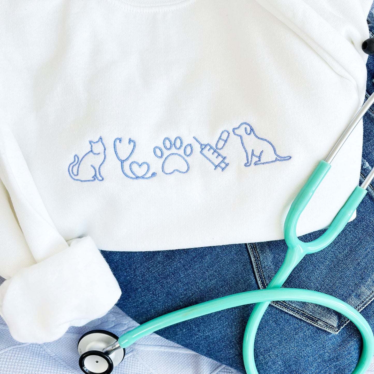 white crewneck sweatshirt with custom embroidered veterinarian icons in a periwinkle thread