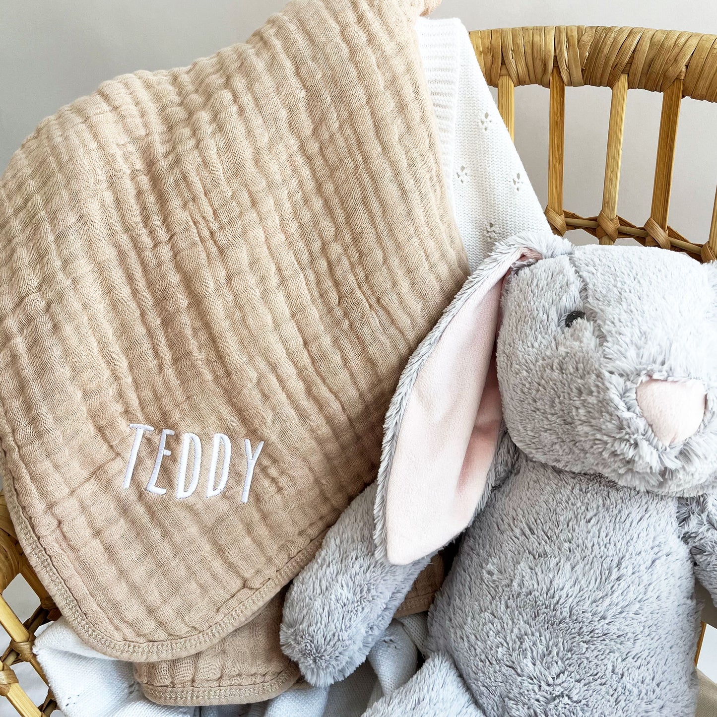 rabbit stuffed animal and sand muslin baby blanket featuring a custom name embroidered design draped over a wicker chair