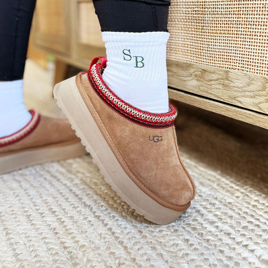 Woman wearing platform Ugg slides and white midi crew socks with custom embroidered staggered initials in Ivy green thread.