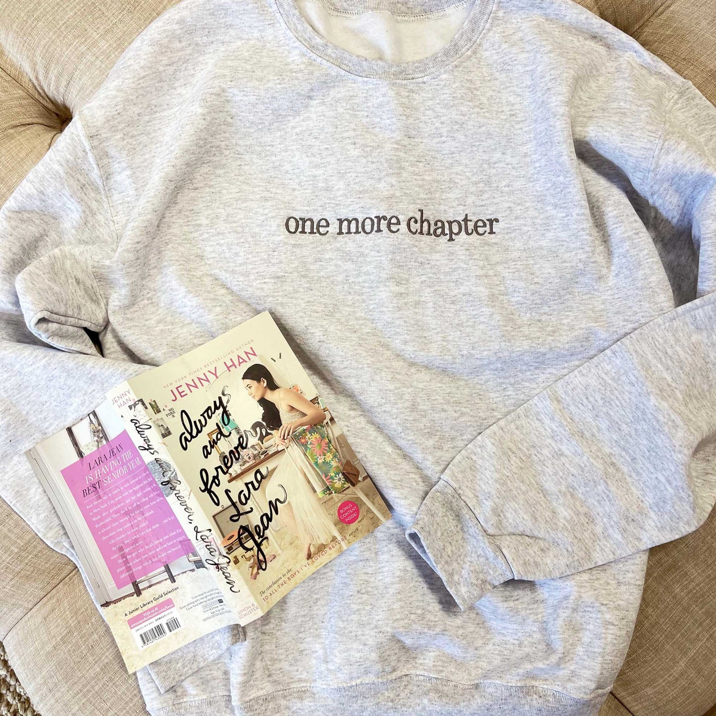 "one more chapter" embroidered sweatshirt flat lay next to book