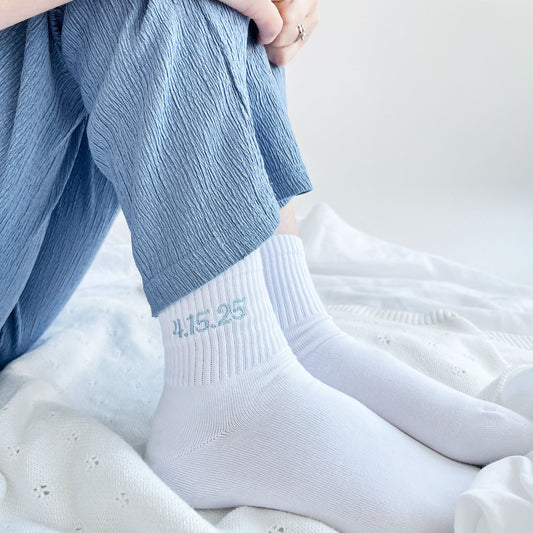 woman wearing blue pajama bottoms and white ankle socks with a custom embroidered date in a powder blue thread