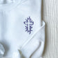 white crewneck sweatshirt with a floral cross embroidered on the left chest in smoky orchid thread