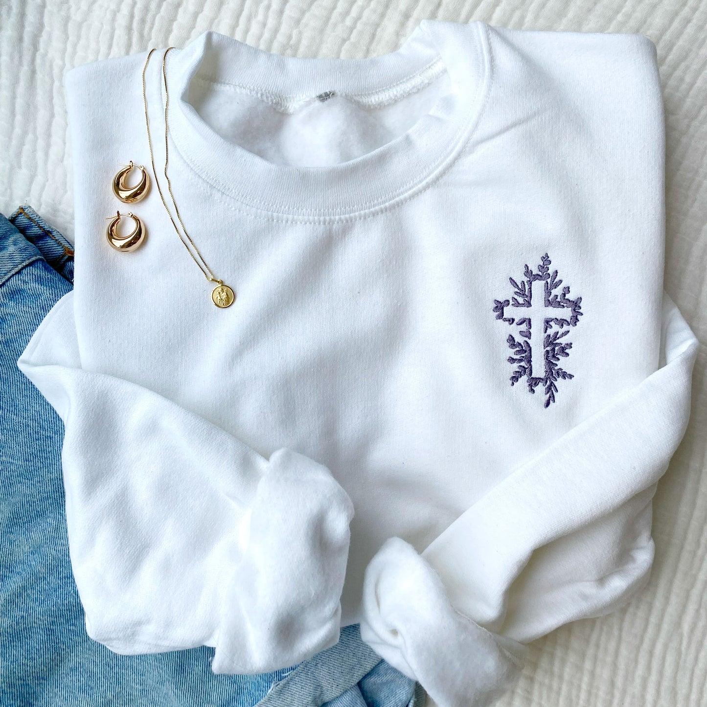 white crewneck sweatshirt with embroidered floral greens that outline a cross. Embroidered in smoky orchid thread