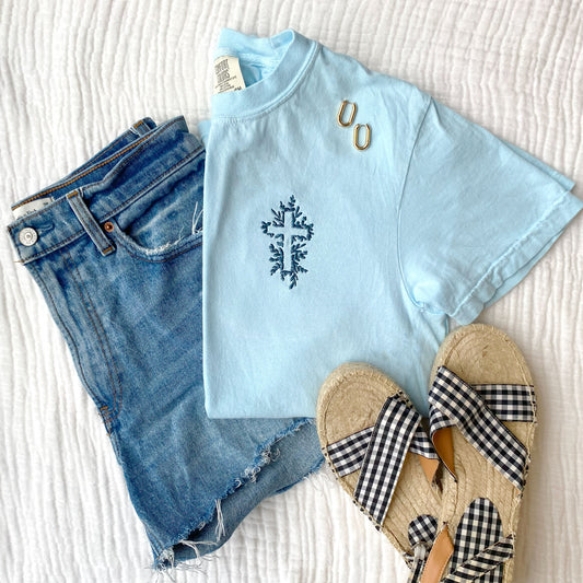 flay lay of jeans, sandals, jewelry, and a chambray comfort colors  t-shirt with a floral embroidered cross in french blue thread 