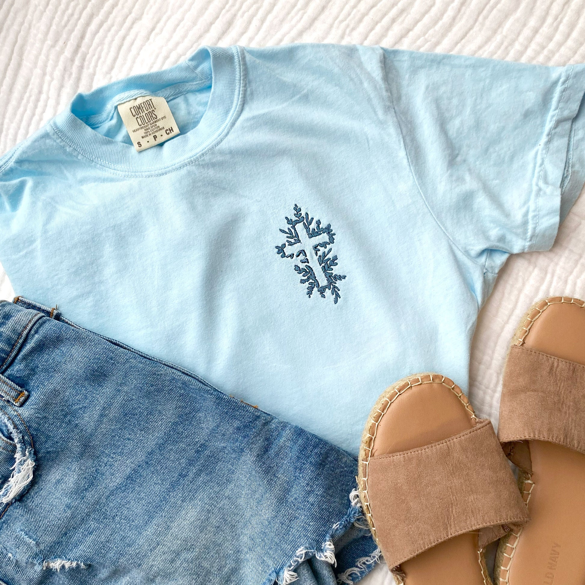 chambray comfort colors t-shirt with a floral embroidered cross in french blue thread and a pair of jean shorts sstyled with sandals