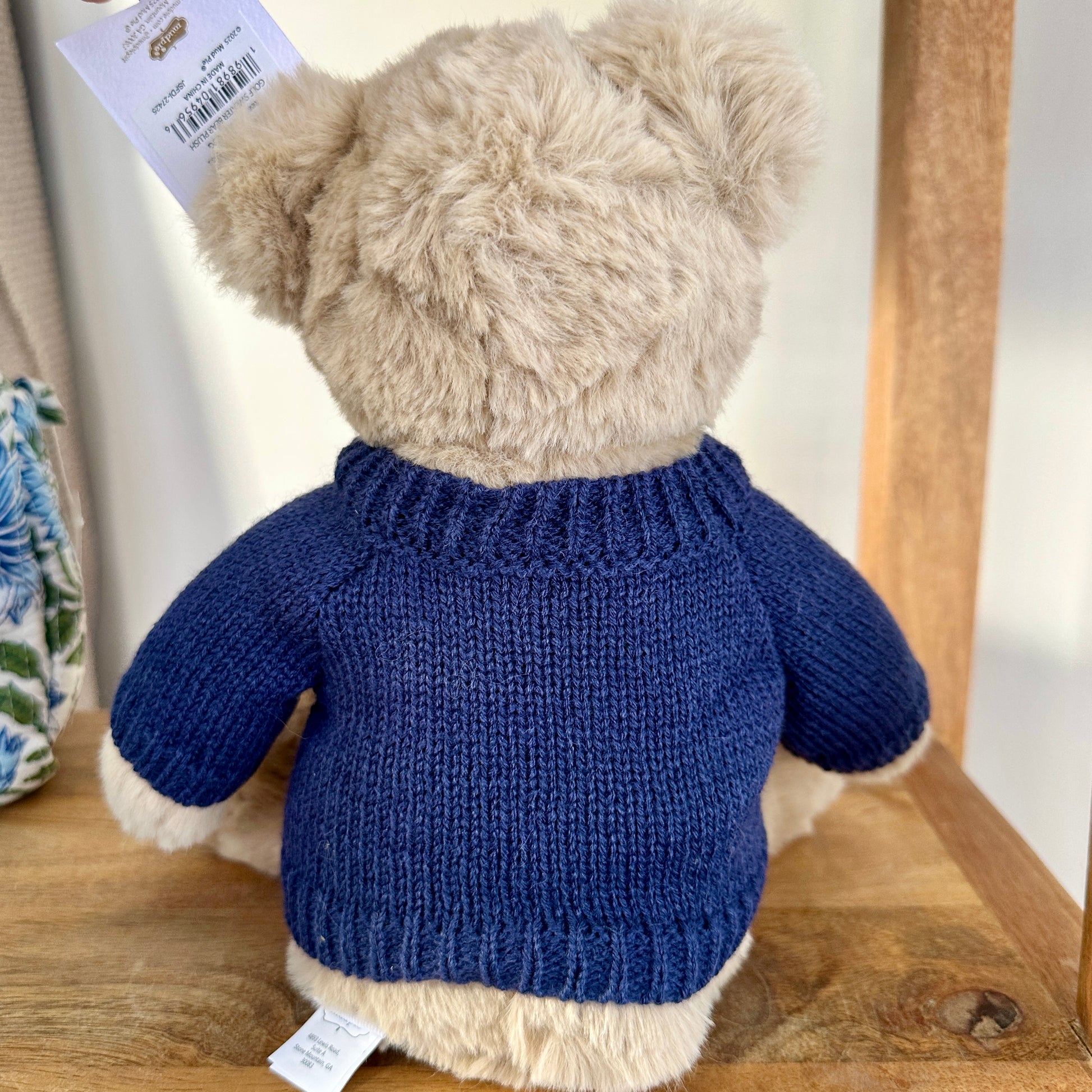 Teddy bear wearing a blue knitted sweater on a wooden surface