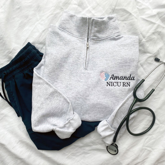 grey quarter zip sweatshirt for a NICU nurse with a personalized embroidered design featuring mini baby feet, name, and credentials.