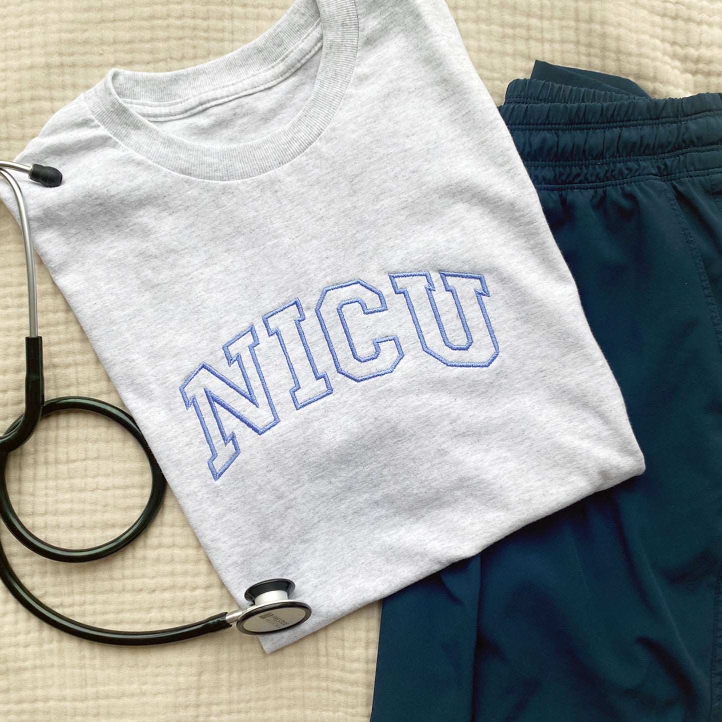 light grey crewneck tee with NICU embroidered in an outlined varsity font across the chest in a periwinkle thread