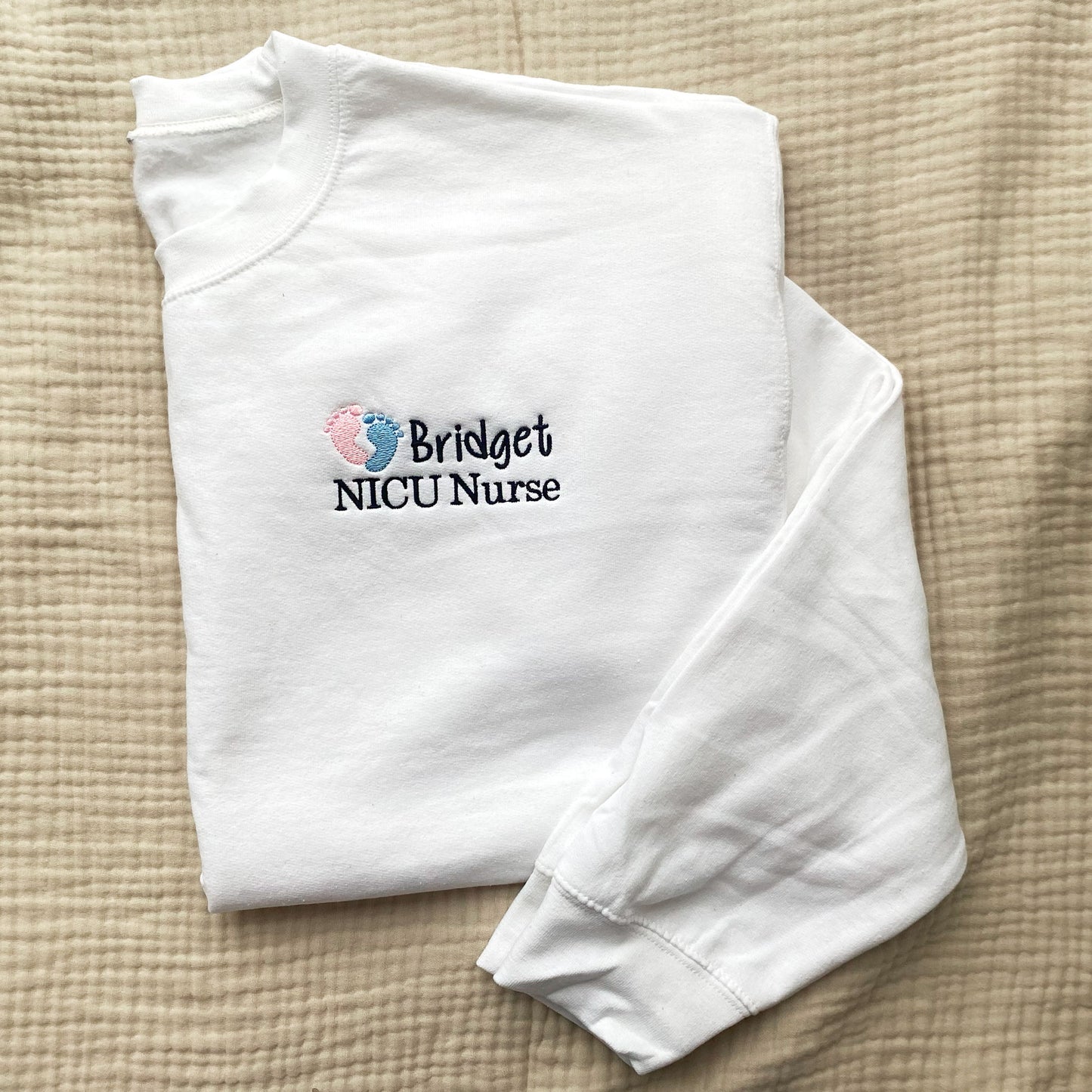 white crewneck sweatshirt  with embroidered nicu design with pink and blue baby feet and custom name and credentials in black thread