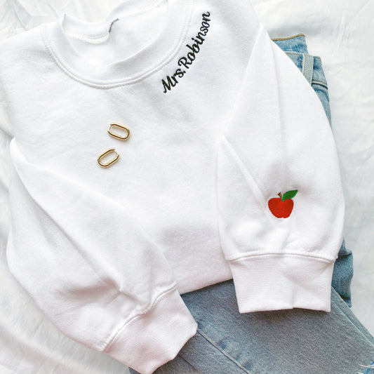 white crewneck sweatshirt for a teacher with collar name embroidery and a mini apple on the cuff