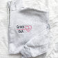 up close flat lay of an Ash quarterzip sweatshirt with custom nurse heart and heartbeat design in pink and name in credentials in black thread