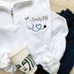 white quarter zip pullover sweatshirt with a custom name and mini heart stethoscope embroidered design on the left chest.