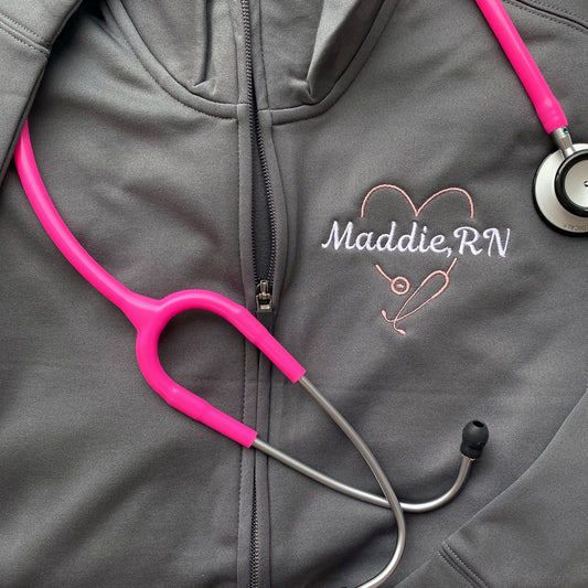 closeup of a grey polyester full zip with a cadet collar and a personalized heart shaped stethoscope and name embroidered design on the left chest.