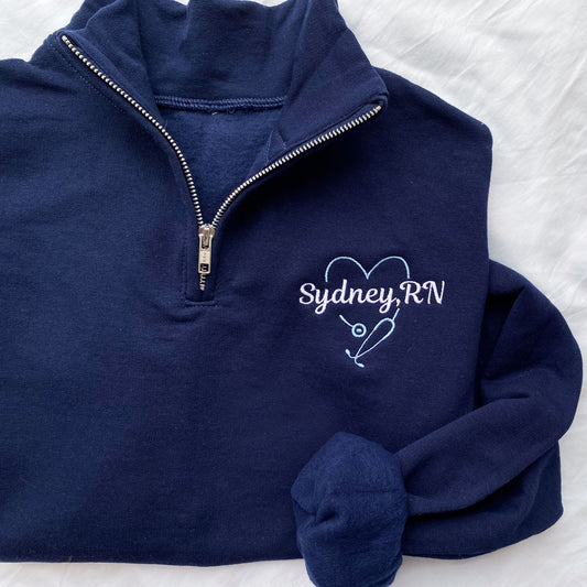 navy blue quarter zip sweatshirt with large heart stethoscope embroidered design with a name through the center