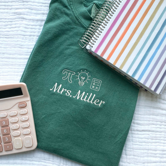 a light green comfort colors tshirt with small embroidered math teacher icons and custom name underneath in natural thread