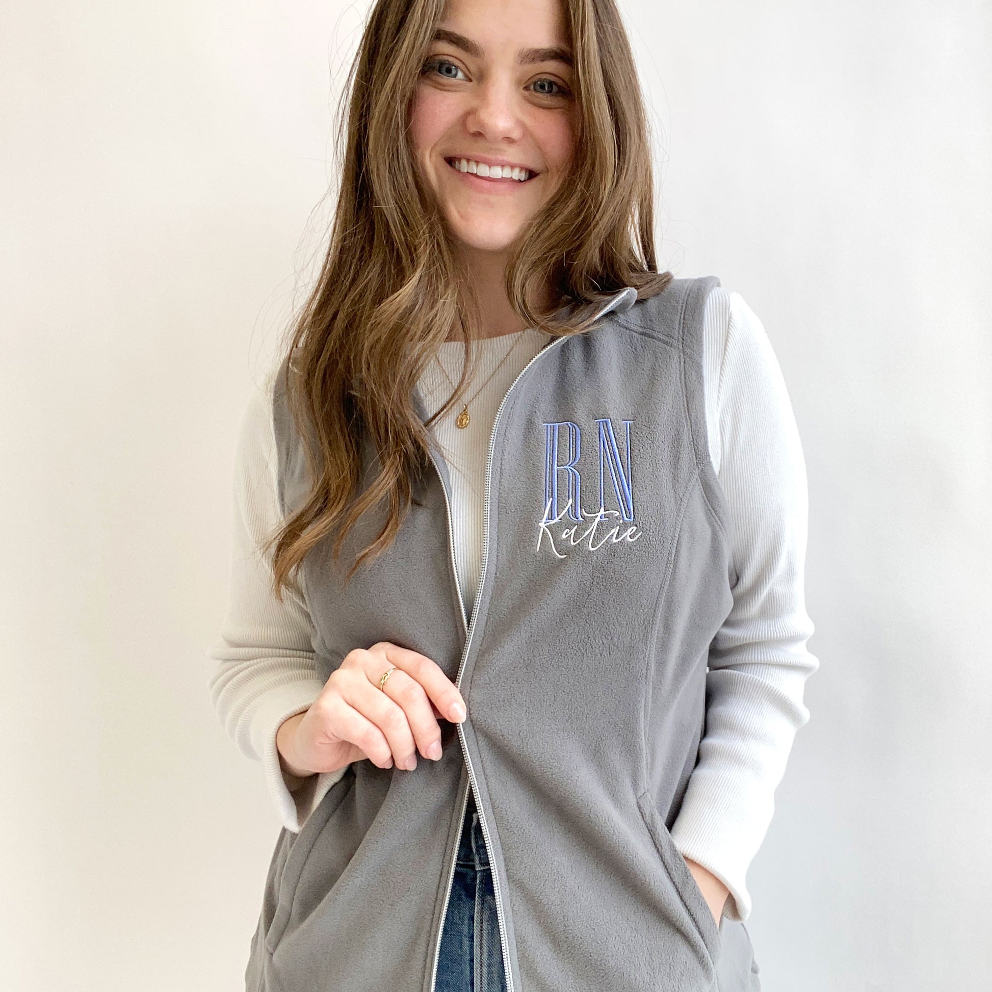 young woman modeling a grey fleece nurse vest with personalized RN design on the left chest in periwinkle and white threads