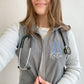selfie of a young woman wearing a grey flecce vest with personalized RN embroidered design 