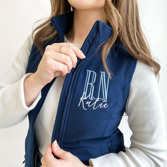 young woman wearing a navy soft shell vest with personalized RN embroidered design