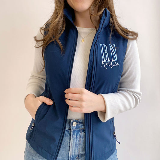 young woman wearing a navy soft shell vest with personalized RN embroidered design on the left chest