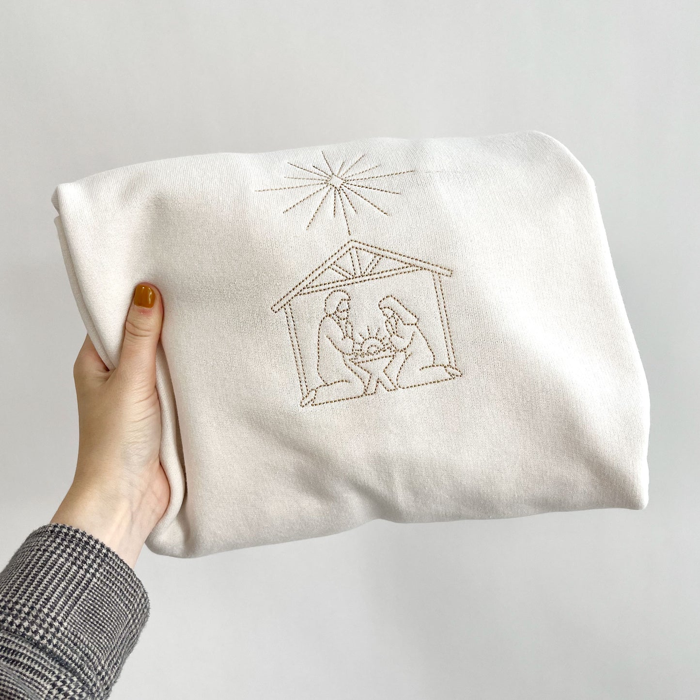 sweet cream crew neck sweatshirt with embroidered stitched nativity scene on the center chest in camel thread.