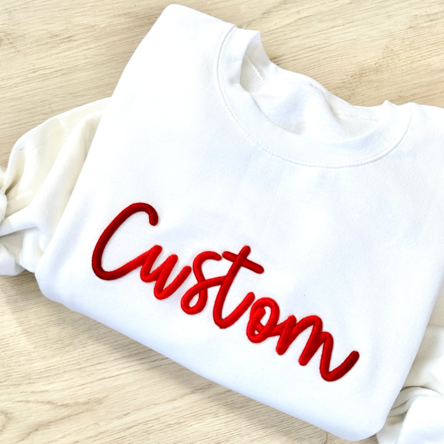 White sweatshirt with red 'Custom' text on a wooden surface