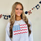 girl wearing an oversized ash crewneck sweatshirt with large embroidered American flag design on the front center chest. Flag is designed with blue bows instead of stars, and scalloped raspberry pink and baby pink stripes in place of the traditional stripes on a flag