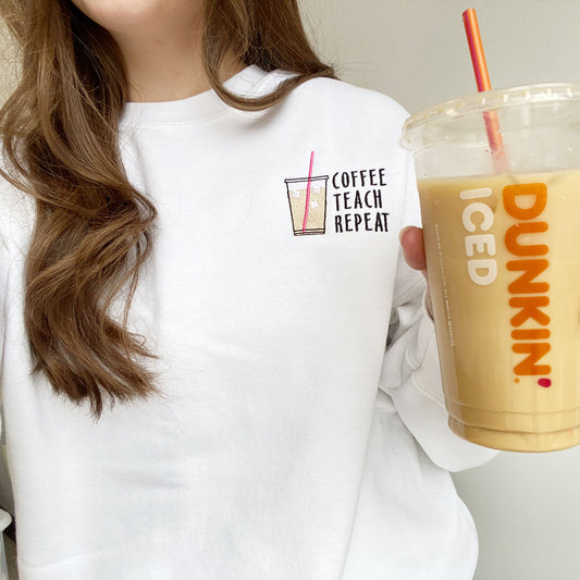 woman wearing a white crewneck sweatshirt with iced coffee and coffee, teach, repeat embroidered on the left chest