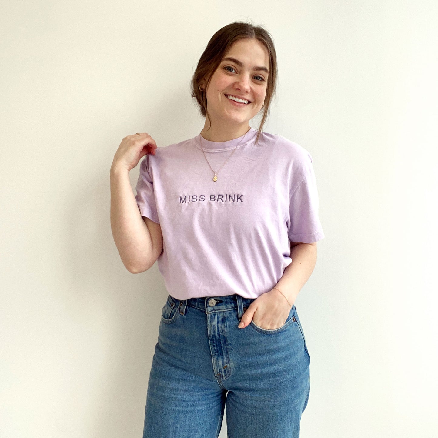 young woman modeling an orchid comfort colors t-shirt with minimal custom embroidered name across the chest in smoky orchid thread