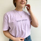 young woman wearing an orchid comfort colors t-shirt with custom all caps minimal name embroidery in smoky orchid thread