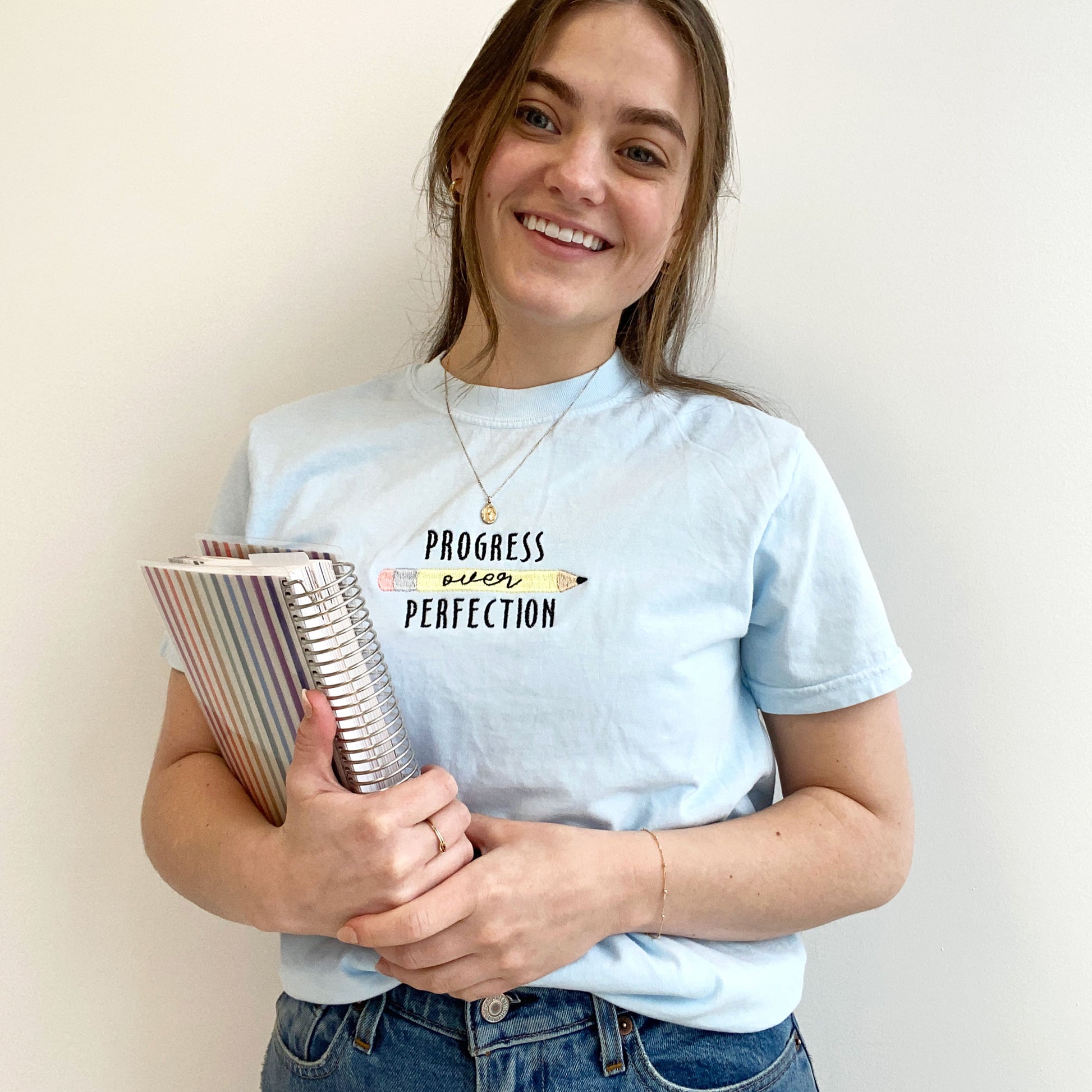 young woman modeling a chambray comfort colors tshirt with embroidered progress over perfection and pencil design