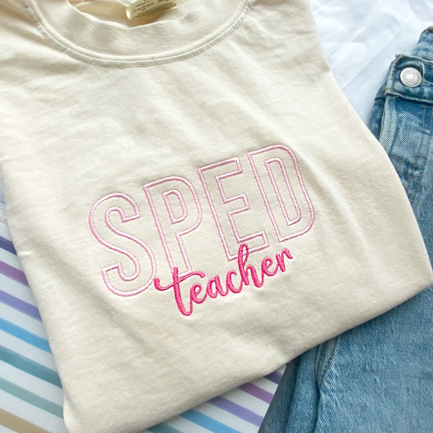 close up of a comfort colors ivory tshirt with embroidered sped teacher design in baby pink and pink threads