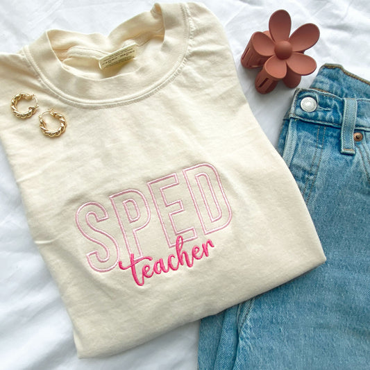 comfort colors ivory tshirt with embroidered sped teacher design in baby pink and pink threads styled with jeans, jewelry and a claw clip