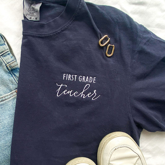 styled flat lay of a navy comfort colors tshirt with personalized grade level and teacher  embroidered design in white thread