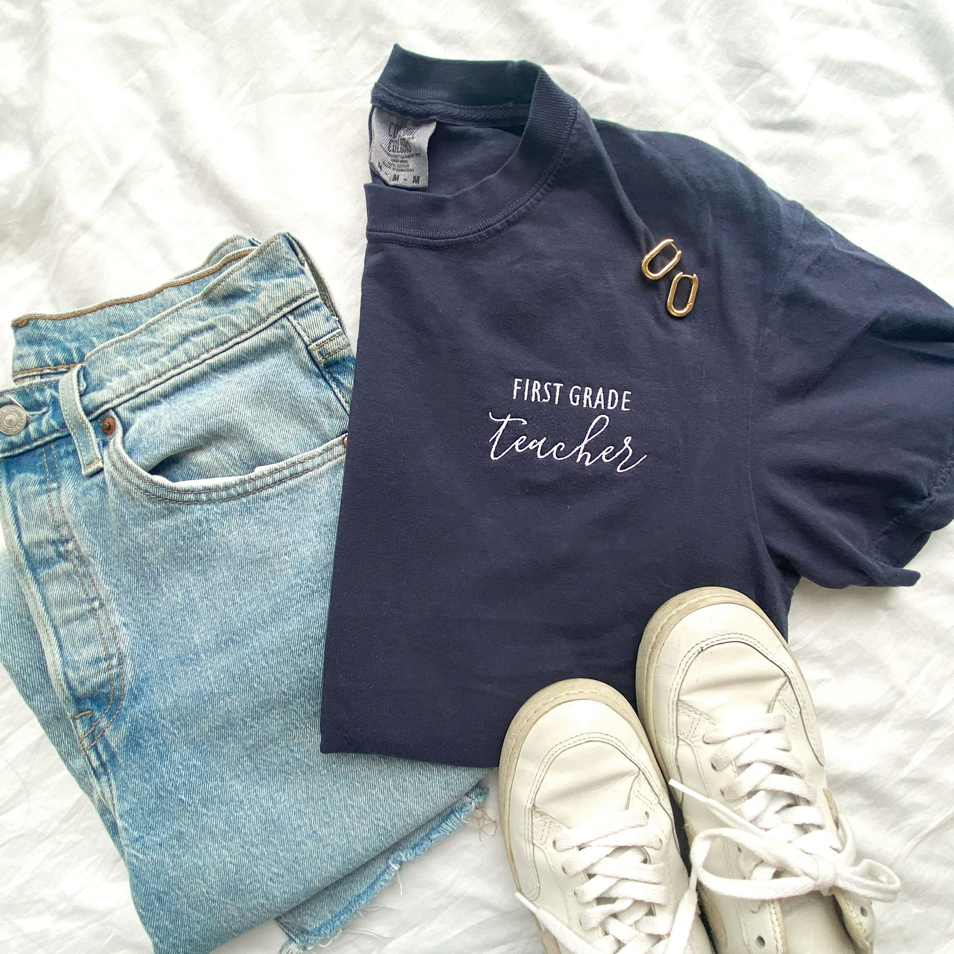 styled flat lay of a navy comfort colors tshirt with personalized grade level and teacher embroidered design in white thread