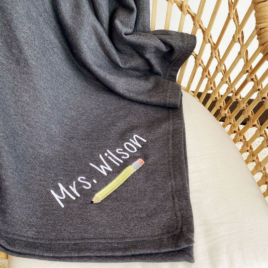 cozy sweatshirt blanket with custom name and pencil embroidered design on the corner