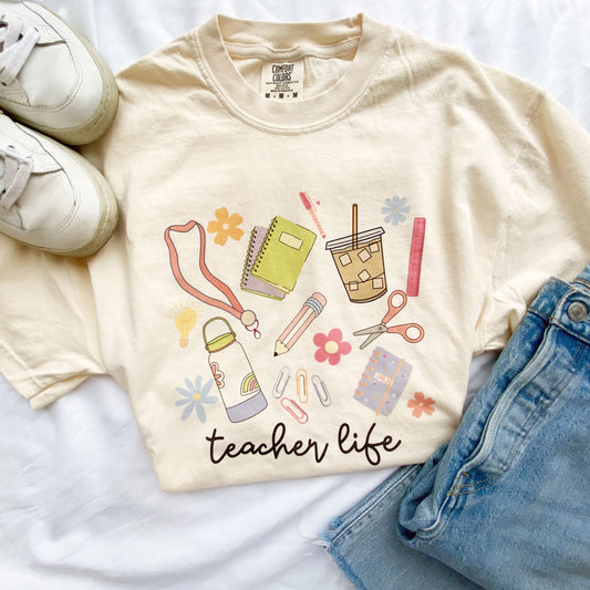 teacher outfit layout featuring blue jeans, flower claw clip, earrings, and an ivory comfort colors t-shirt with a fun teacher life school supplies print
