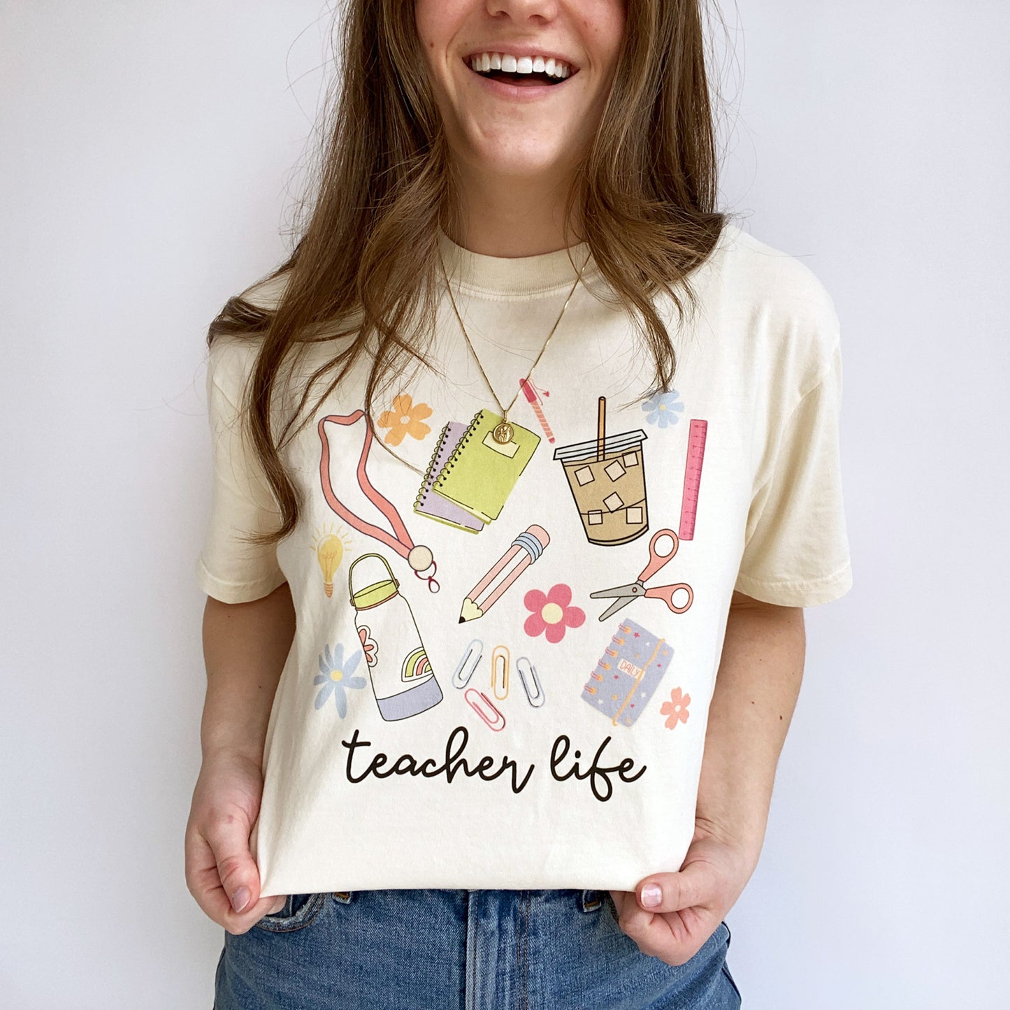 teacher wearing an ivory t-shirt with a school supplies teacher life printed design