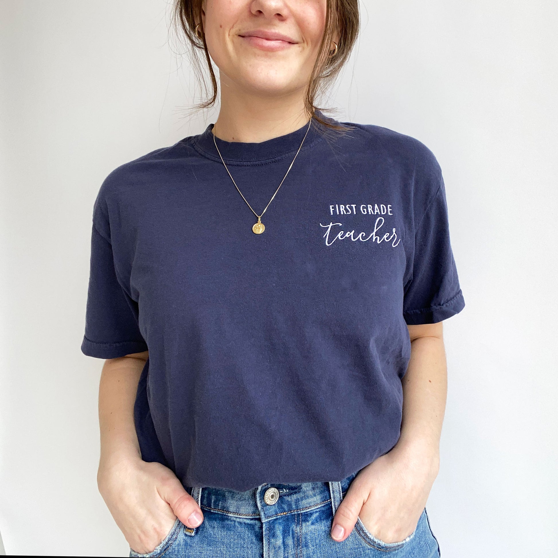 young woman modeling a nay comfort colors t-shirt with embroidered custom grade level and teacher design in white threads on the left chest