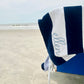 navy blue and white striped cabana beach towel with custom name embroidery in a cursive blithe font along the second stripe, horizontally. Embroidery is in powder blue thread. Towel is draped over a low sitting beach chair on a sandy beach with the ocean in front