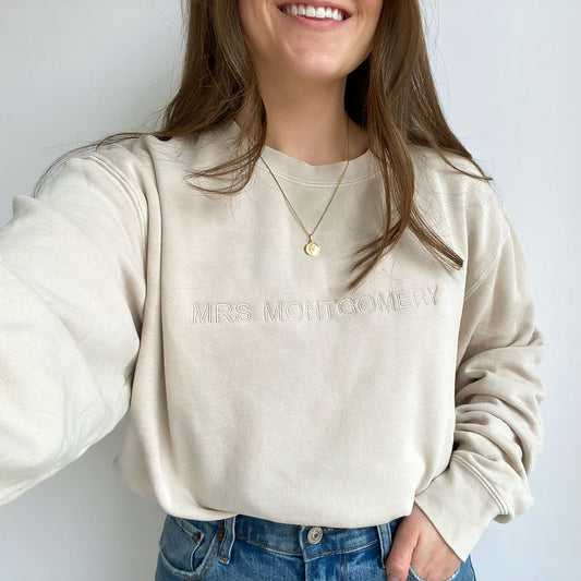 young woman modeling an ivory crewneck sweatshirt with mininmal embroidered name in all caps across the chest in natural thread