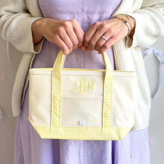 Person holding a beige tote bag with yellow gingham pattern and initials 'JBM' on a plain background