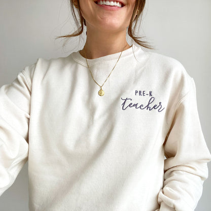 young woman wearing a sweet cream crewneck sweatshirt with custom teacher grade design embroidered in smoky orchid thread