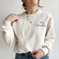 young woman wearing a sweet cream crewneck sweatshirt with custom teacher grade design embroidered in smoky orchid thread