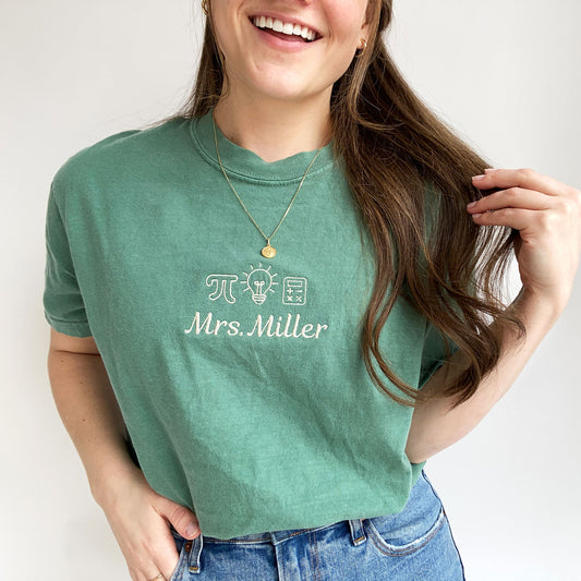 young woman wearing s=a light green comfort colors tshirt with small embroidered math teacher icons and custom name underneath in natural thread