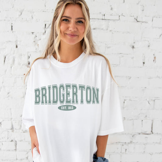 girl wearing an oversized white comfort colors t-shirt with a large bridgerton print in a varsity inspired font.