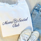white crewneck sweatshirt styled with jeans and sneakers. On the sweatshirt is embroidered Moms Social club design with little coffee cup in navy threads