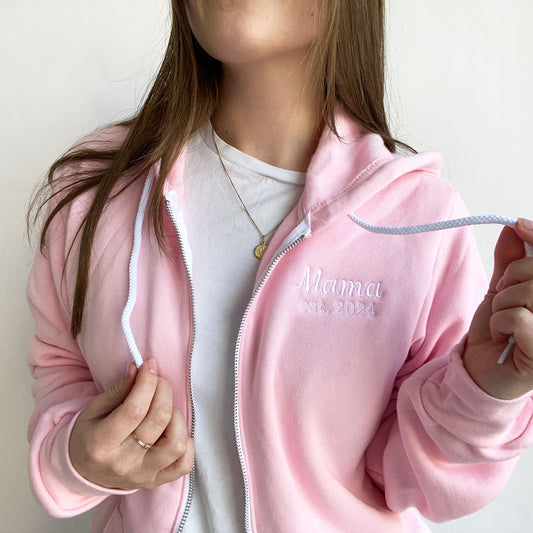 close up of a young woman wearing a pink bella and canvas full zip jacket with embroidered Mama est 2024 design on the left chest in white thread